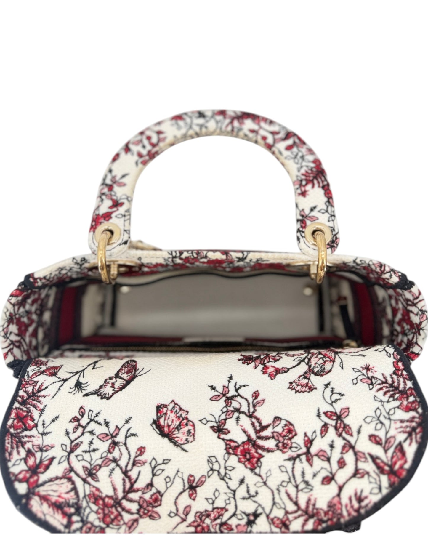 A structured handbag with a cream-colored base and an intricate red and black floral embroidery pattern, featuring gold-tone hardware and top handles.