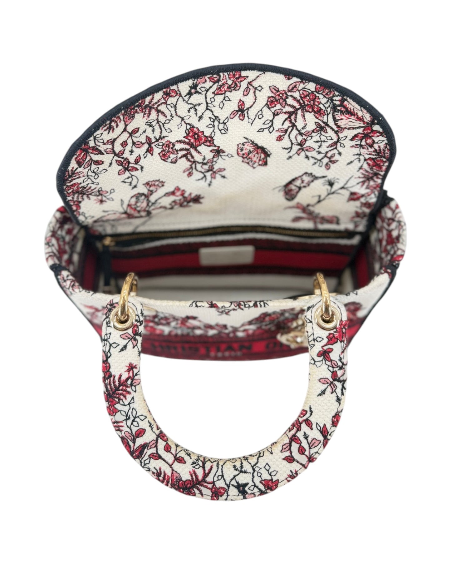 A top-down view of a small handbag with a cream-colored fabric body decorated with a red and black floral vine pattern. It features two small top handles connected by a matching fabric loop, gold-tone hardware, and a striped interior lining.