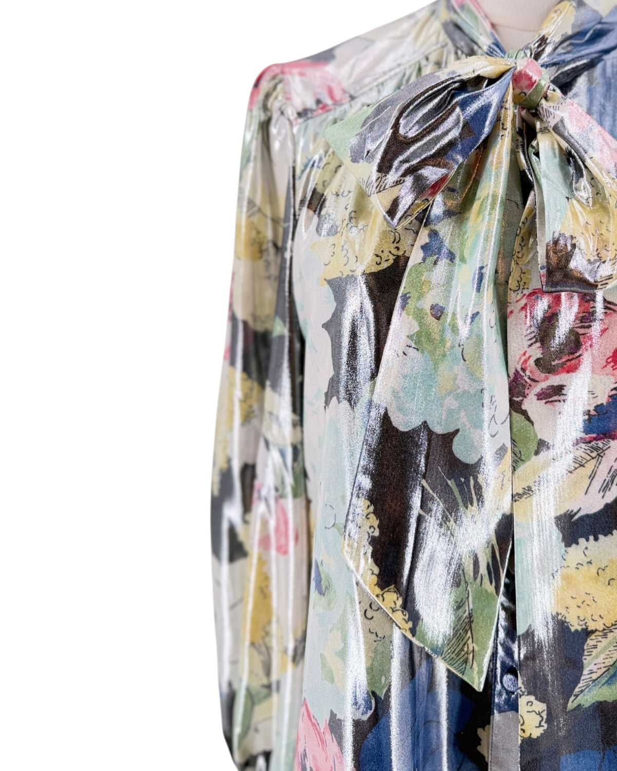 A close-up of a shiny, multicolor floral print dress with a large bow at the collar, featuring a metallic sheen and abstract floral patterns in yellow, green, pink, and blue.