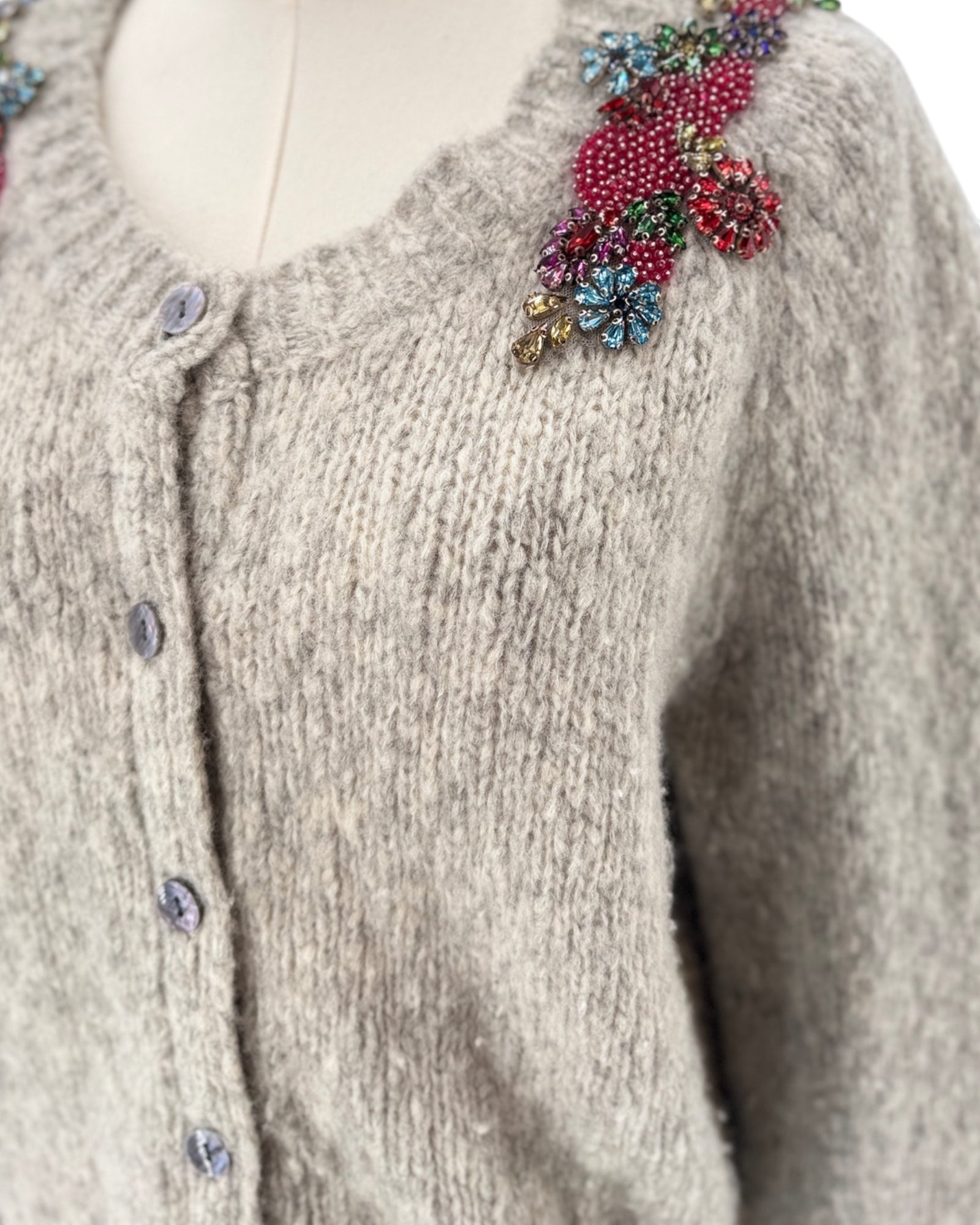 Knitted cardigan with floral embellishments on a mannequin against a white background