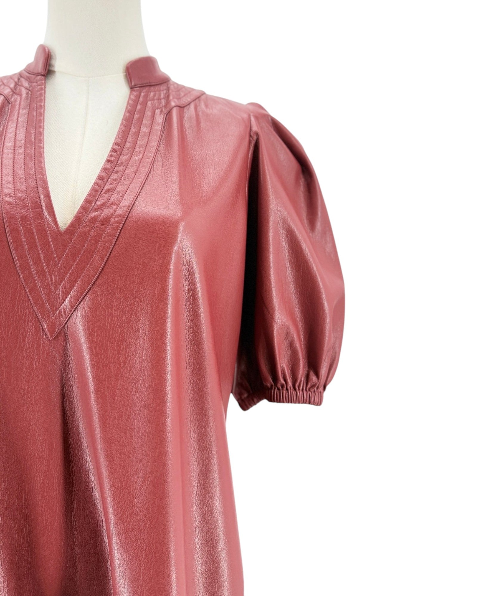A brick red faux leather top with a V-neckline, pleated collar details, and puff sleeves, displayed on a mannequin against a white background.