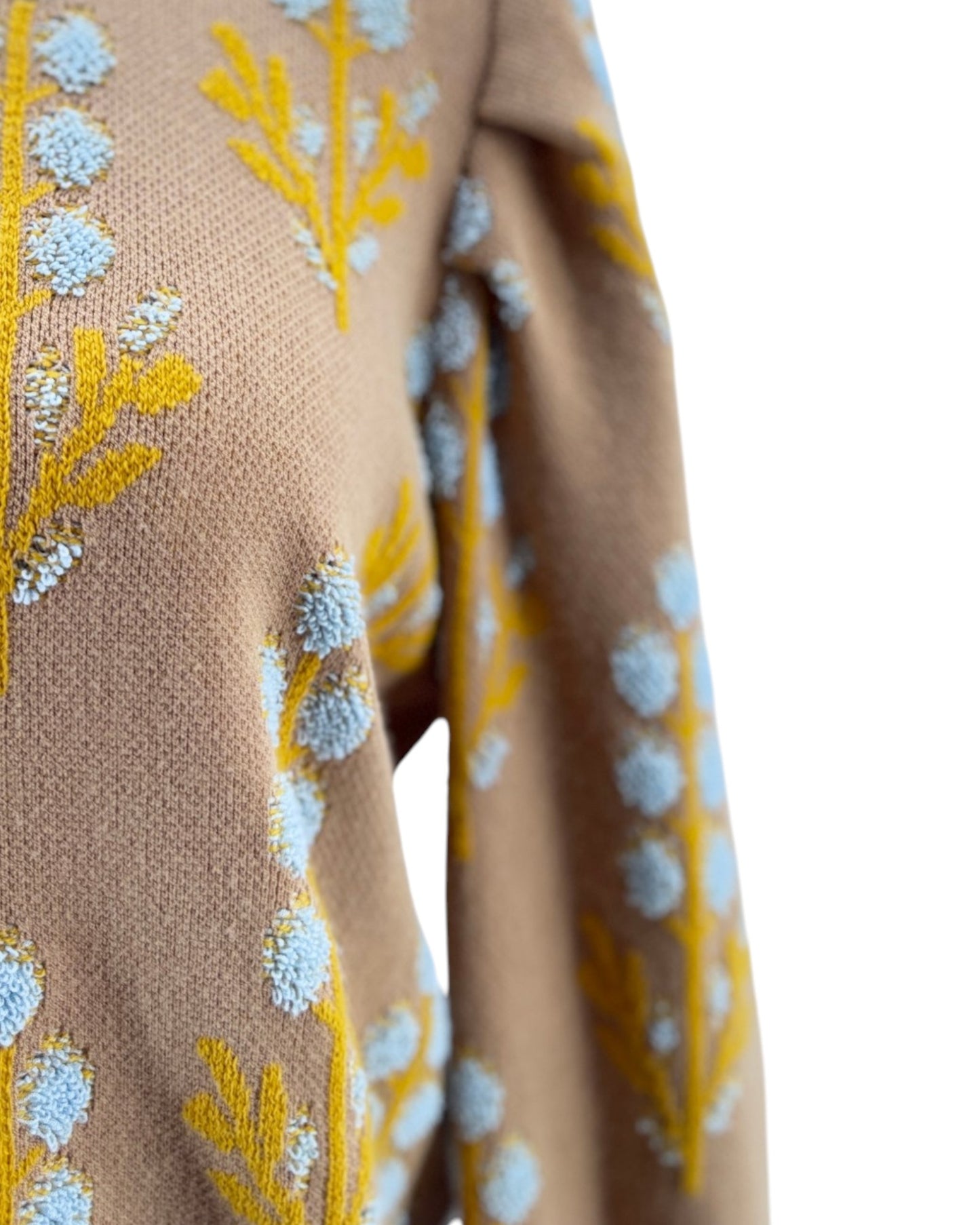Close-up of a beige fabric with yellow and blue floral embroidery on a white background