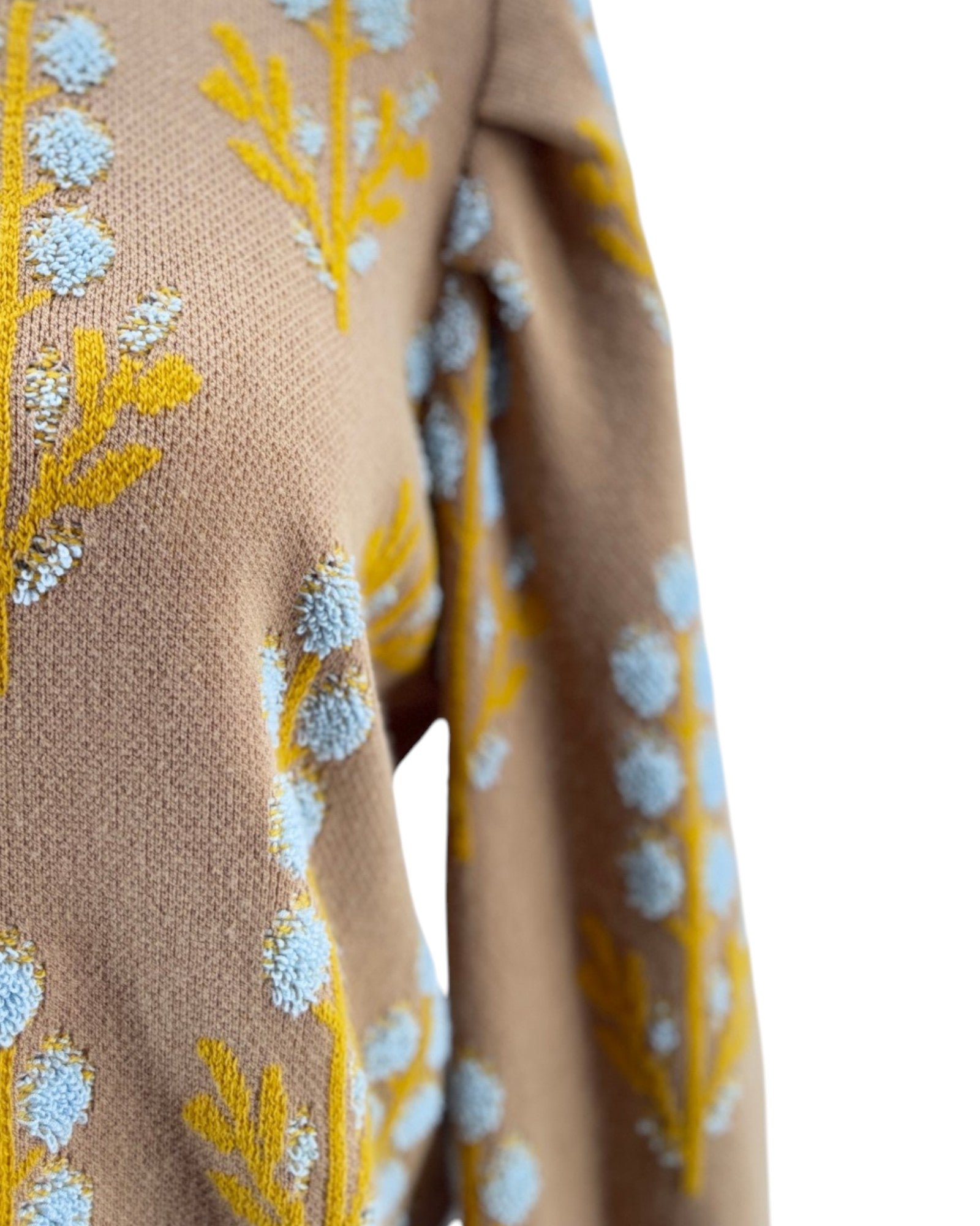 Close-up of a beige fabric with yellow and blue floral embroidery on a white background