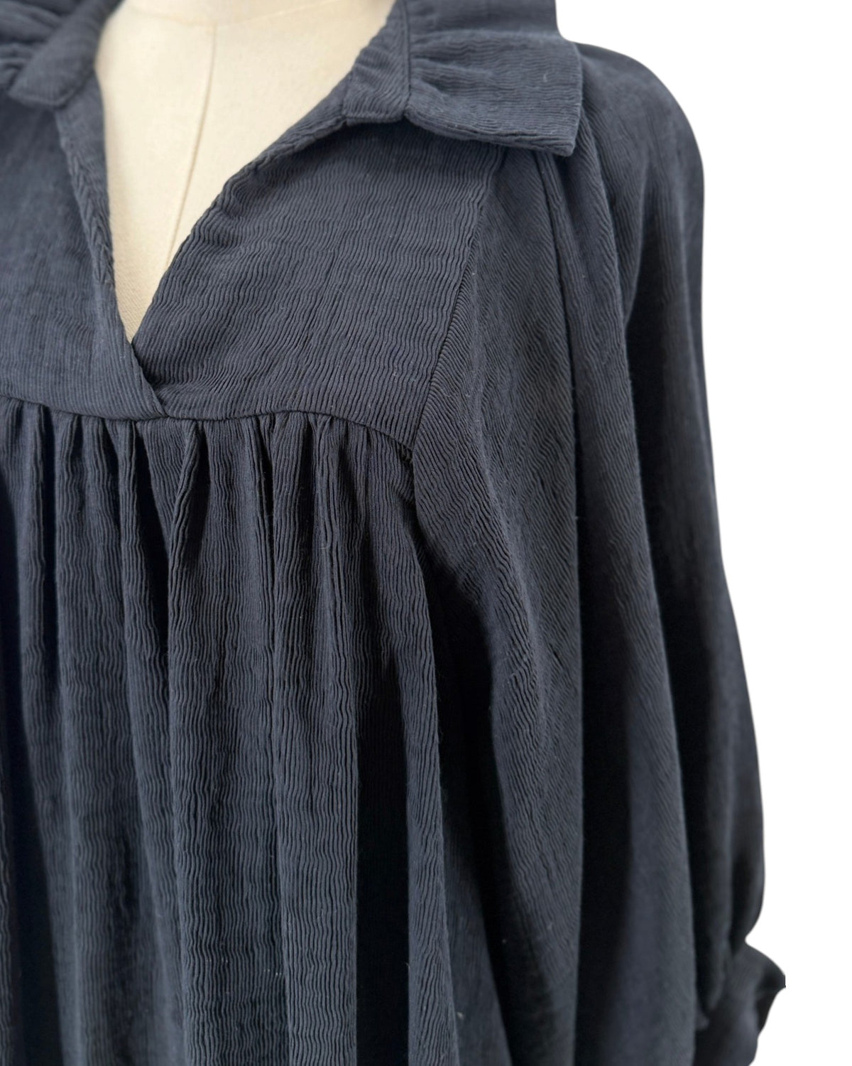 High ruffle stand-up collar, notched v-neck, gathered detailing at the bodice, voluminous loose blouson sleeves, shift silhouette, side pockets on a mannequin on a white background