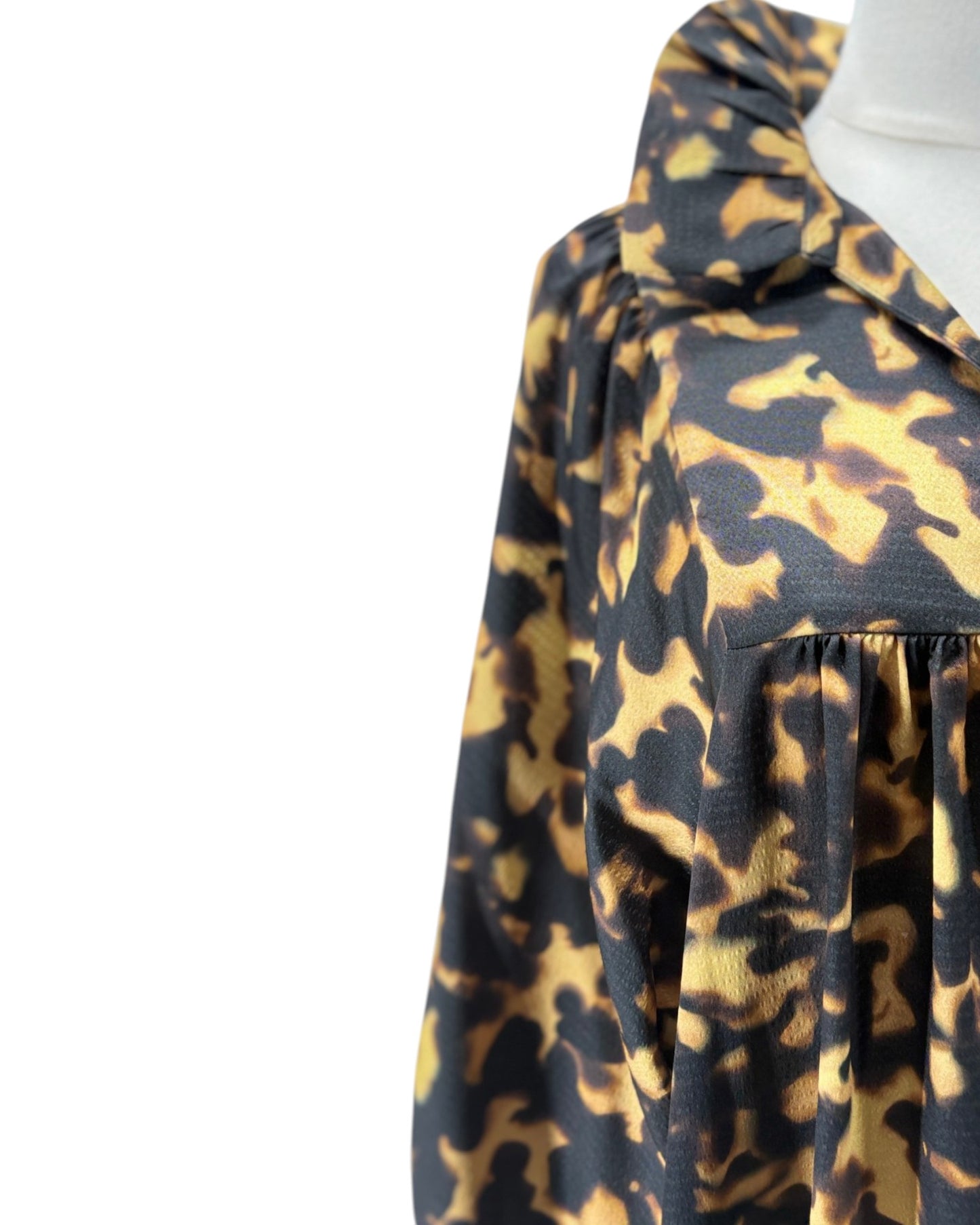 A close-up of a leopard print blouse on a mannequin, featuring a black and tan pattern with a ruffled collar and long sleeves.