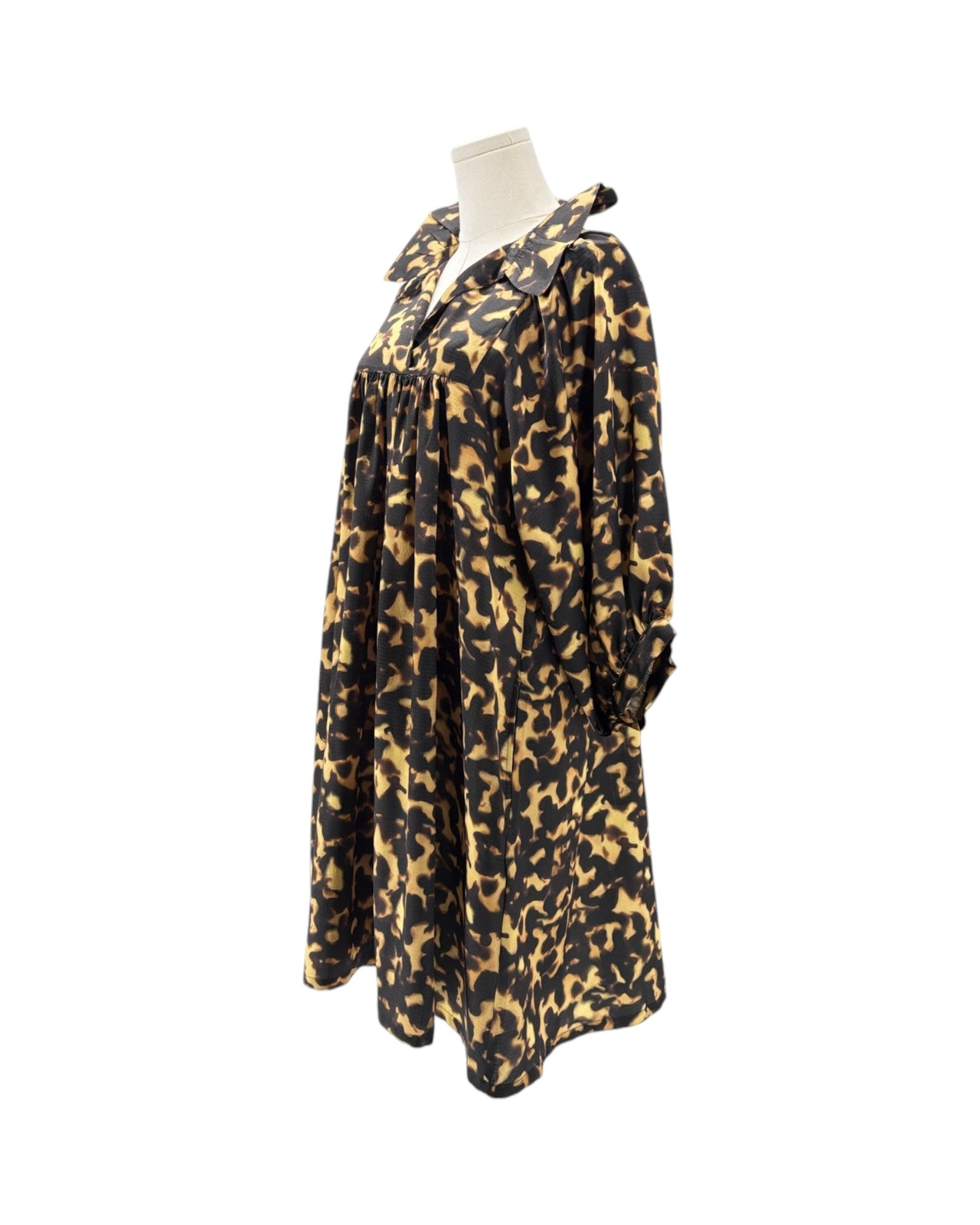 A long-sleeve, loose-fitting tunic dress with a black and tan leopard print pattern, displayed on a mannequin torso against a plain white background.