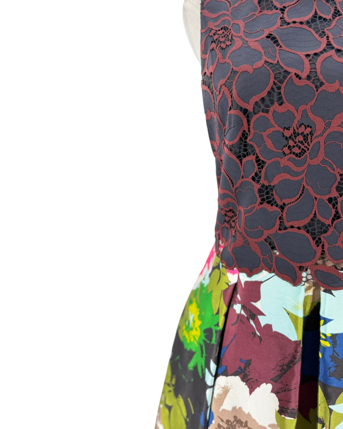 Close-up of a sleeveless dress  featuring a dark navy floral lace overlay on the upper section and a multicolor floral print on the lower section, shown against a plain white background.