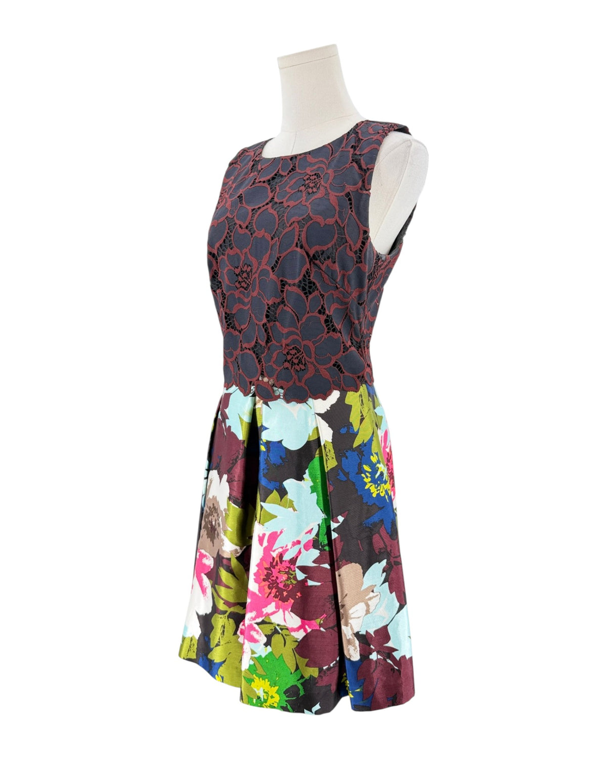 A sleeveless fit-and-flare dress displayed on a mannequin against a white background. The bodice features a dark red and black floral lace overlay, while the flared skirt has a vibrant multicolor floral print with pink, blue, green, and yellow tones.
