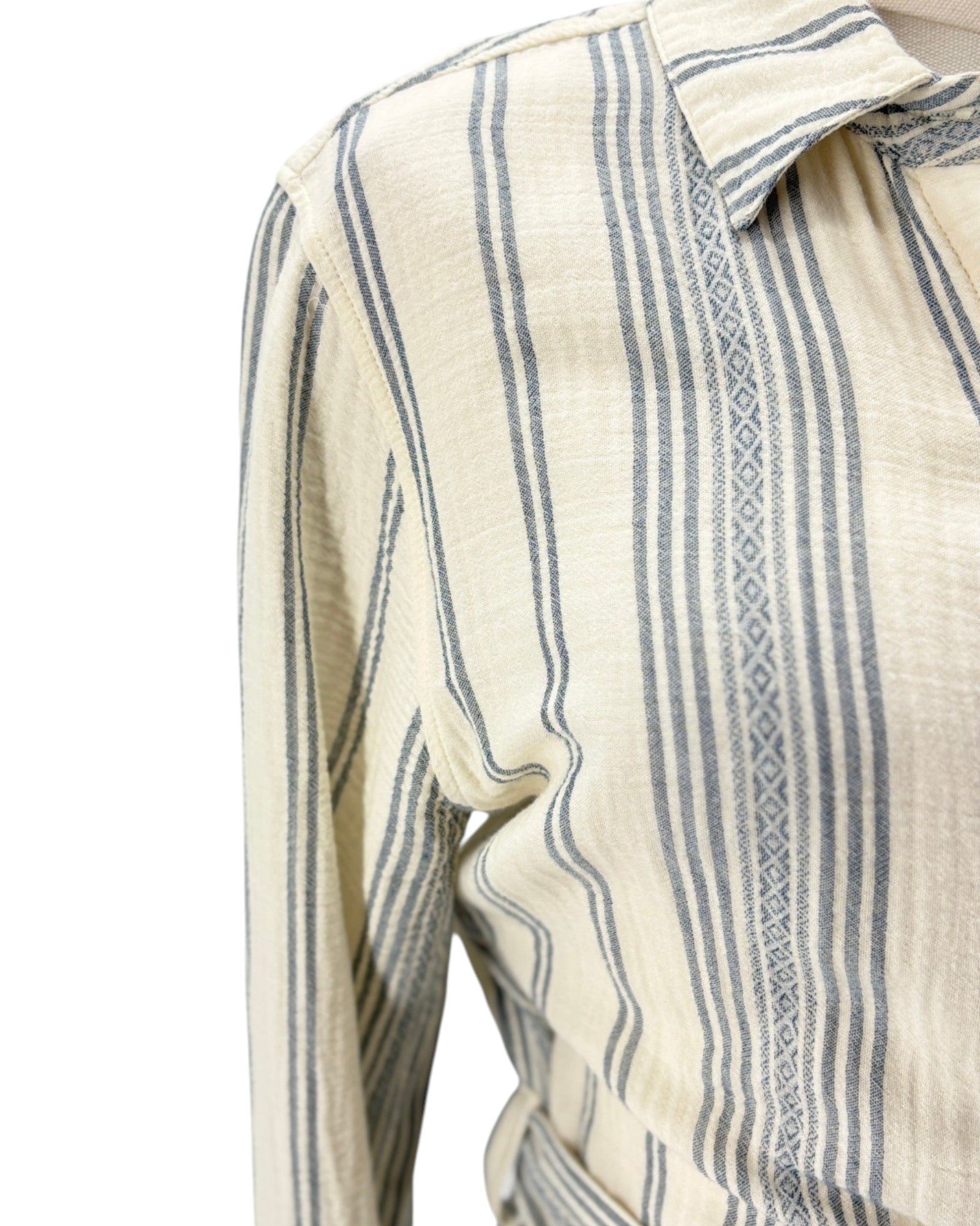 Close-up of a long-sleeve collared shirt with vertical blue-gray stripes on a warm cream base, featuring a subtle woven geometric pattern along the placket.