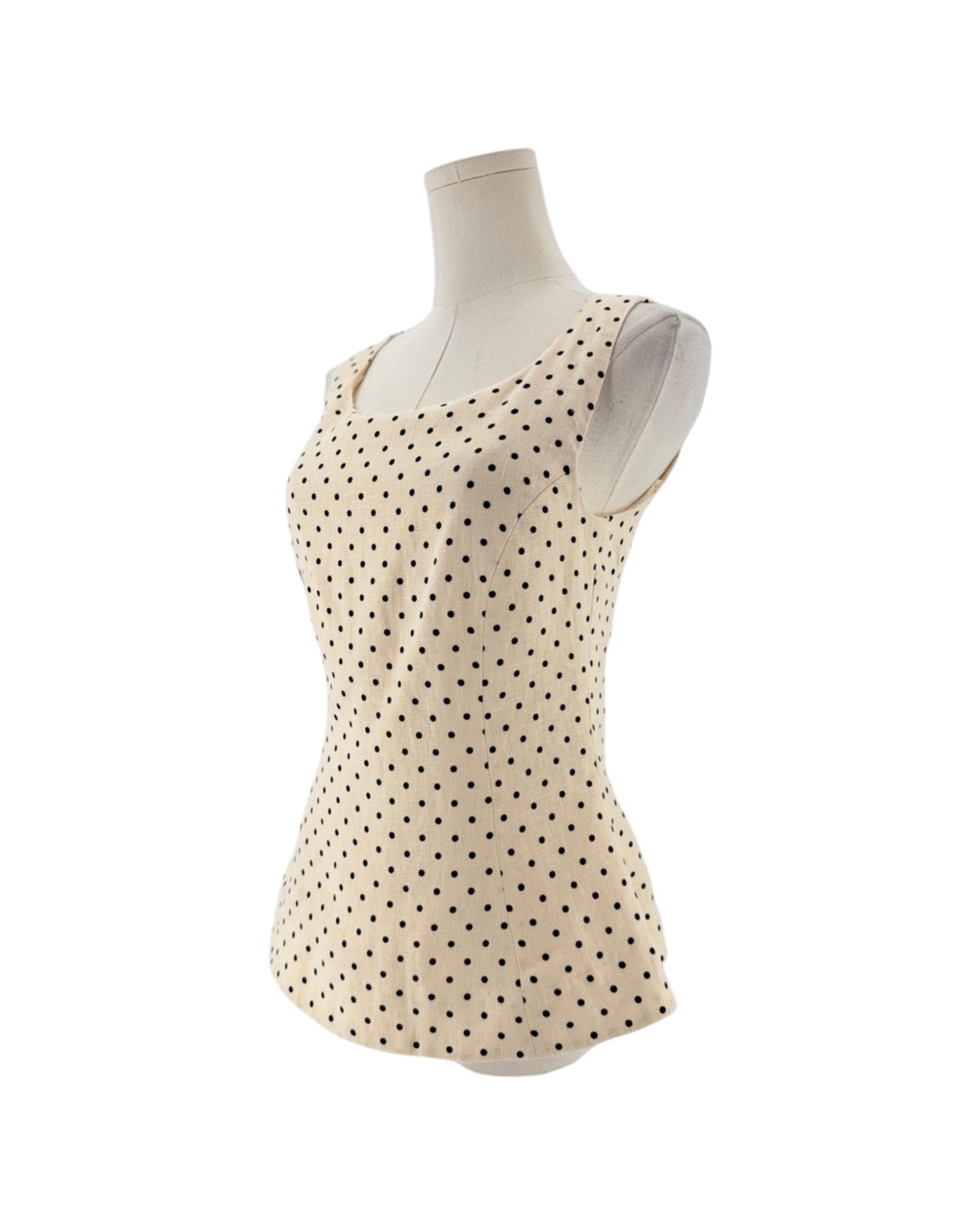 Sleeveless cream peplum top with back polka dots on a mannequin on a white background