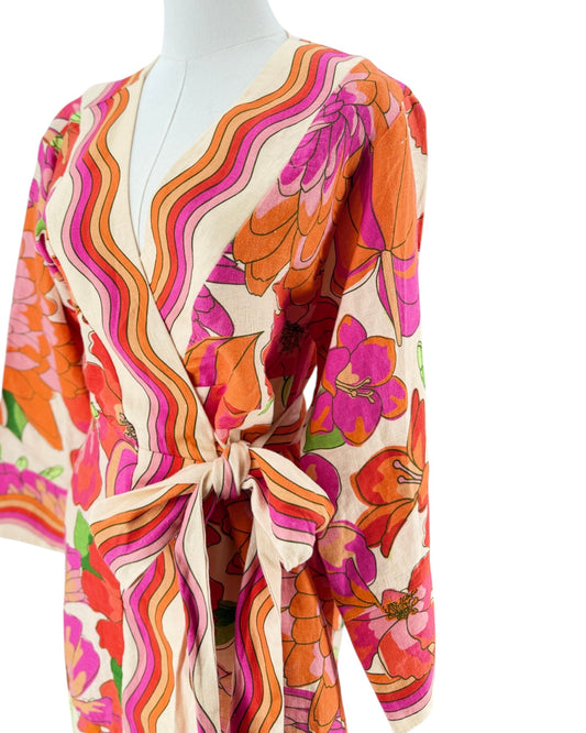 A long-sleeve wrap mini with a tie waist, featuring a vibrant retro floral and wavy stripe pattern in orange, pink, red, and green on a cream background, displayed on a white mannequin torso.