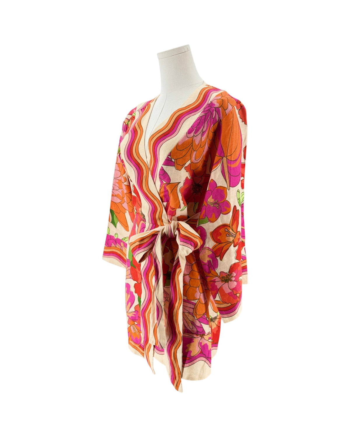 A lightweight wrap-style mini dress with a tie waist, featuring a vibrant retro floral and wavy stripe pattern in orange, pink, purple, and green on a cream background, displayed on a white mannequin torso.