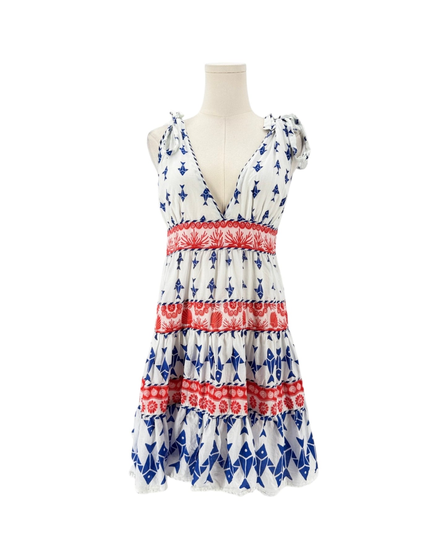 A sleeveless tiered dress displayed on a mannequin torso against a plain white background. The dress has a white base with an allover blue pattern and three horizontal red patterned bands.