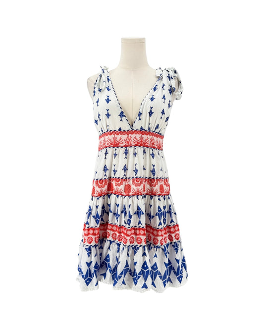 A sleeveless tiered dress displayed on a mannequin torso against a plain white background. The dress has a white base with an allover blue pattern and three horizontal red patterned bands.