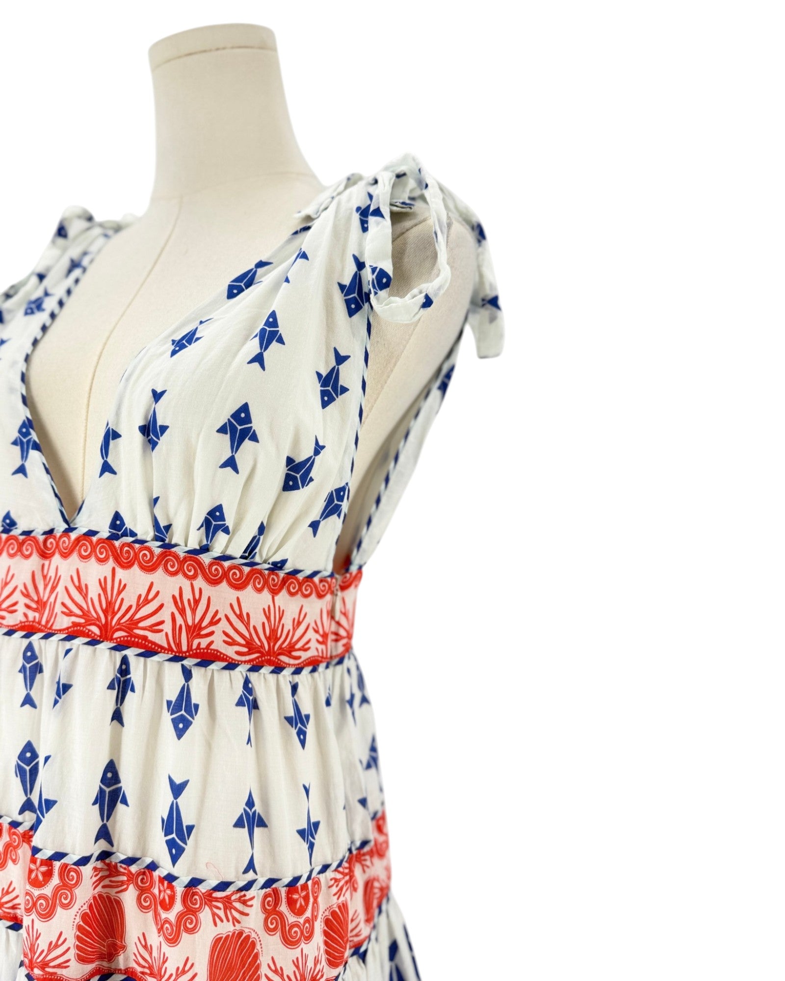 A sleeveless white dress with blue fish prints and red floral bands, displayed on a beige mannequin torso against a white background.