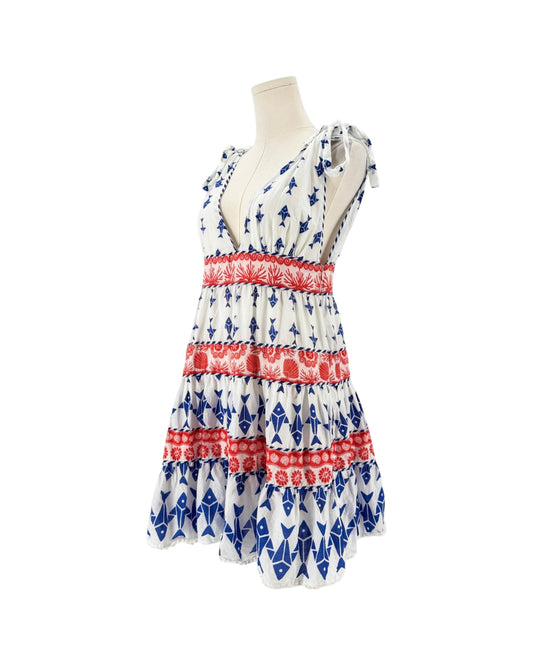 A sleeveless tiered dress displayed on a mannequin torso against a plain white background. The dress has a white base with blue geometric patterns and red horizontal bands.