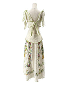 Mannequin wearing a white dress with floral patterns and green accents on a white background