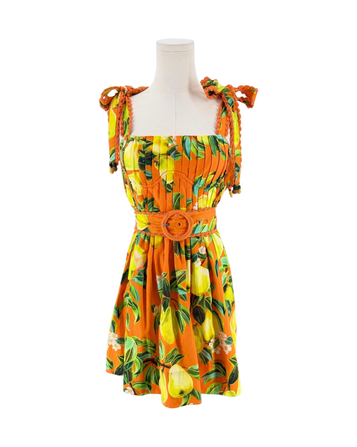 An orange sleeveless dress with a yellow and green lemon print, featuring tie-shoulder straps, a smocked bodice, and a matching orange belt with a round buckle, displayed on a white mannequin torso against a white background.