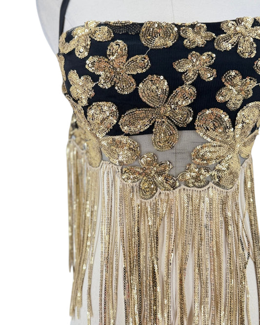 Close-up of a black and gold embellished garment on a mannequin, featuring large sequined floral motifs and long dangling fringe.
