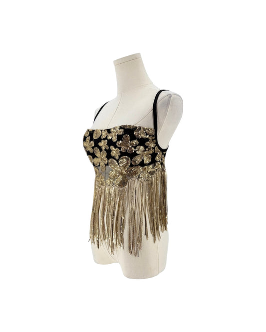 A black and gold embellished sleeveless top with fringe, displayed on a cream mannequin torso against a white background.