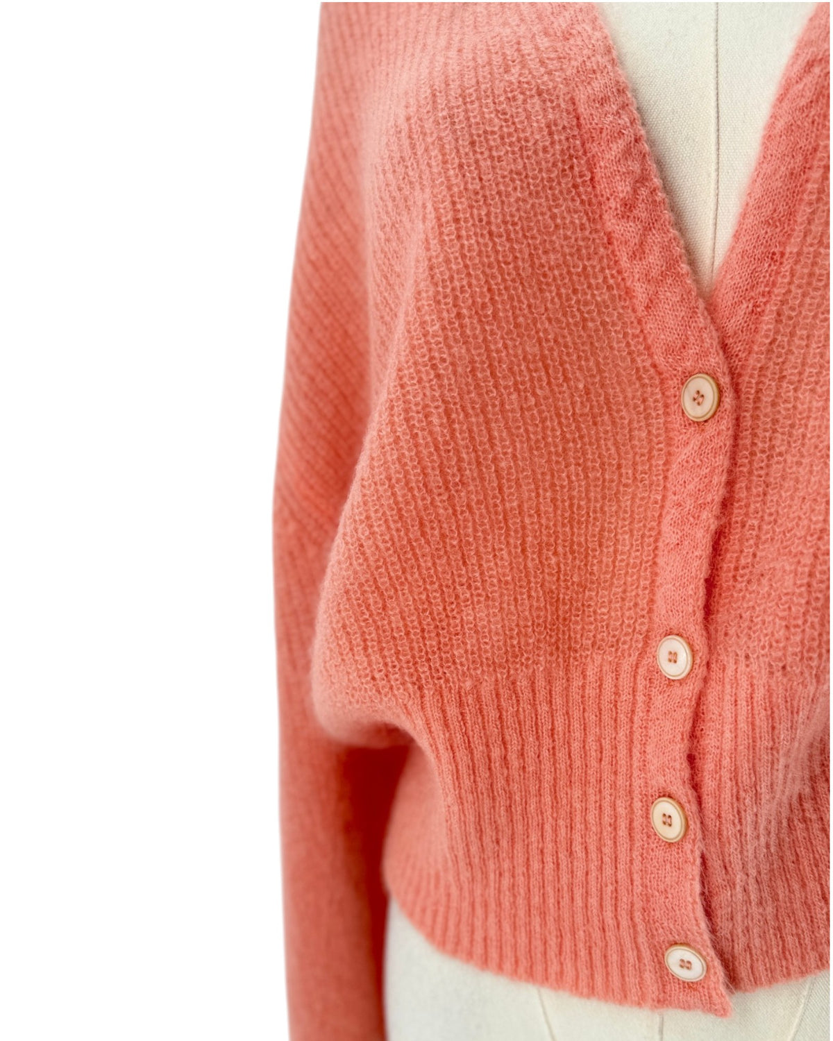 A coral pink knit cardigan sweater displayed on a cream-colored mannequin torso against a plain white background.