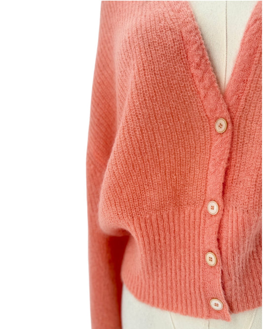 A coral pink knit cardigan sweater displayed on a cream-colored mannequin torso against a plain white background.