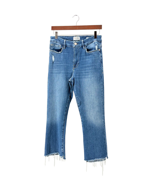 Medium wash blue denim cropped jeans with a distressed front thigh and raw frayed hems, hanging on a wooden hanger against a white background.