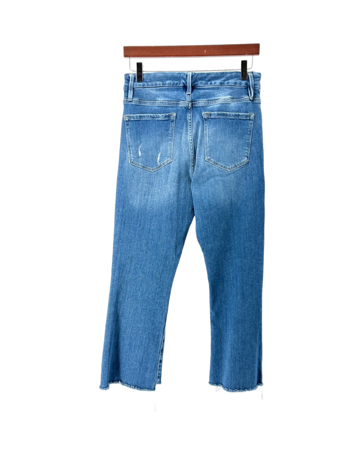 Blue denim jeans shown from the back, hanging from a wooden hanger against a plain white background.