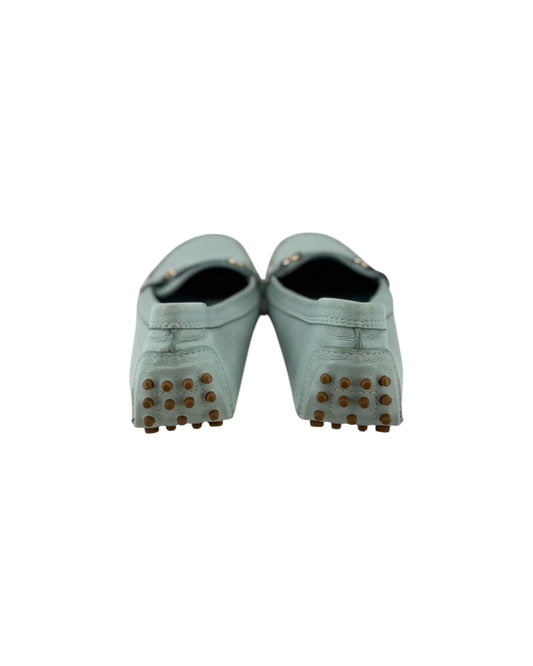 A pair of light Blue green leather mule shoes with brown rubber spikes on the soles, shown from the back against a plain white background.
