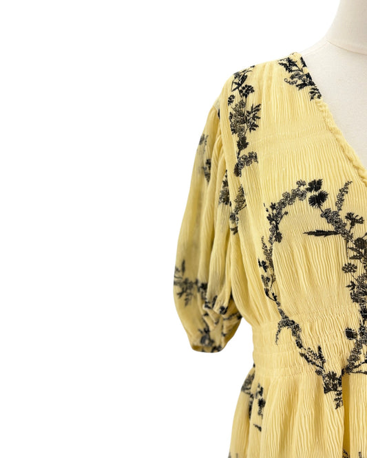 Yellow dress with black floral embroidery on a mannequin against a white background