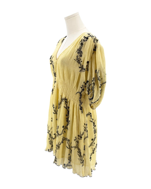 Yellow dress with black floral embroidery on a mannequin against a white background