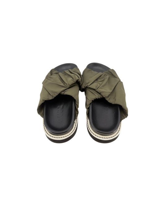 Black slip on sandals with two thick green straps across the top on a white background