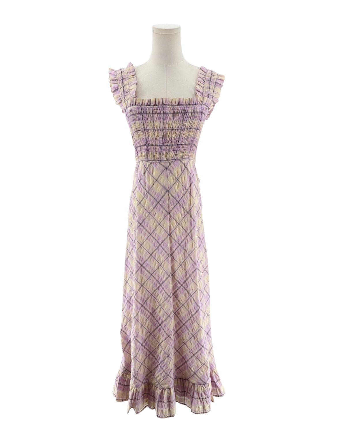 A sleeveless, smocked maxi dress with a purple and beige plaid pattern, displayed on a mannequin against a white background. and ruffle bottom. On a mannequin on a white background.