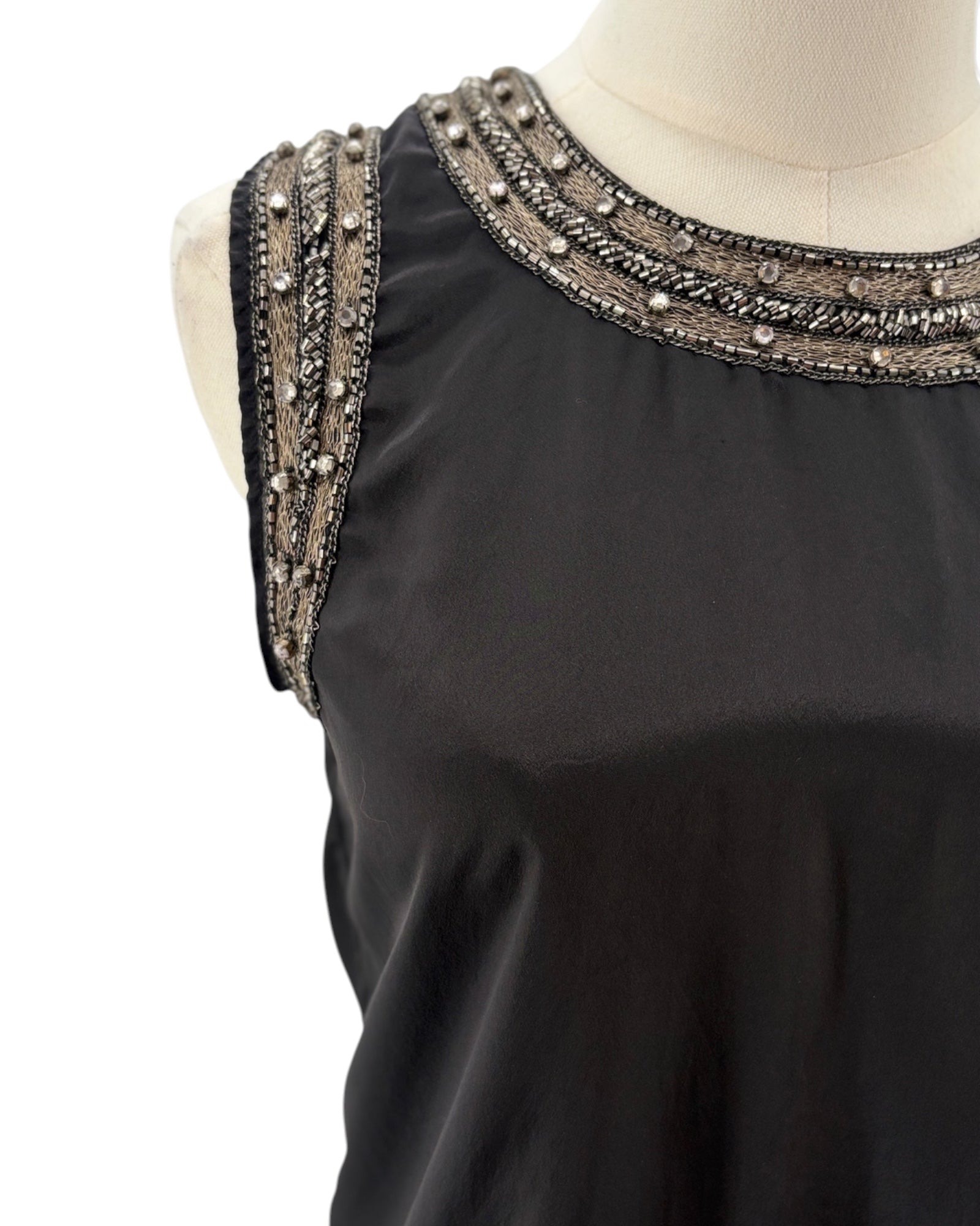 Black top with intricate beaded shoulder details on a mannequin against a white background