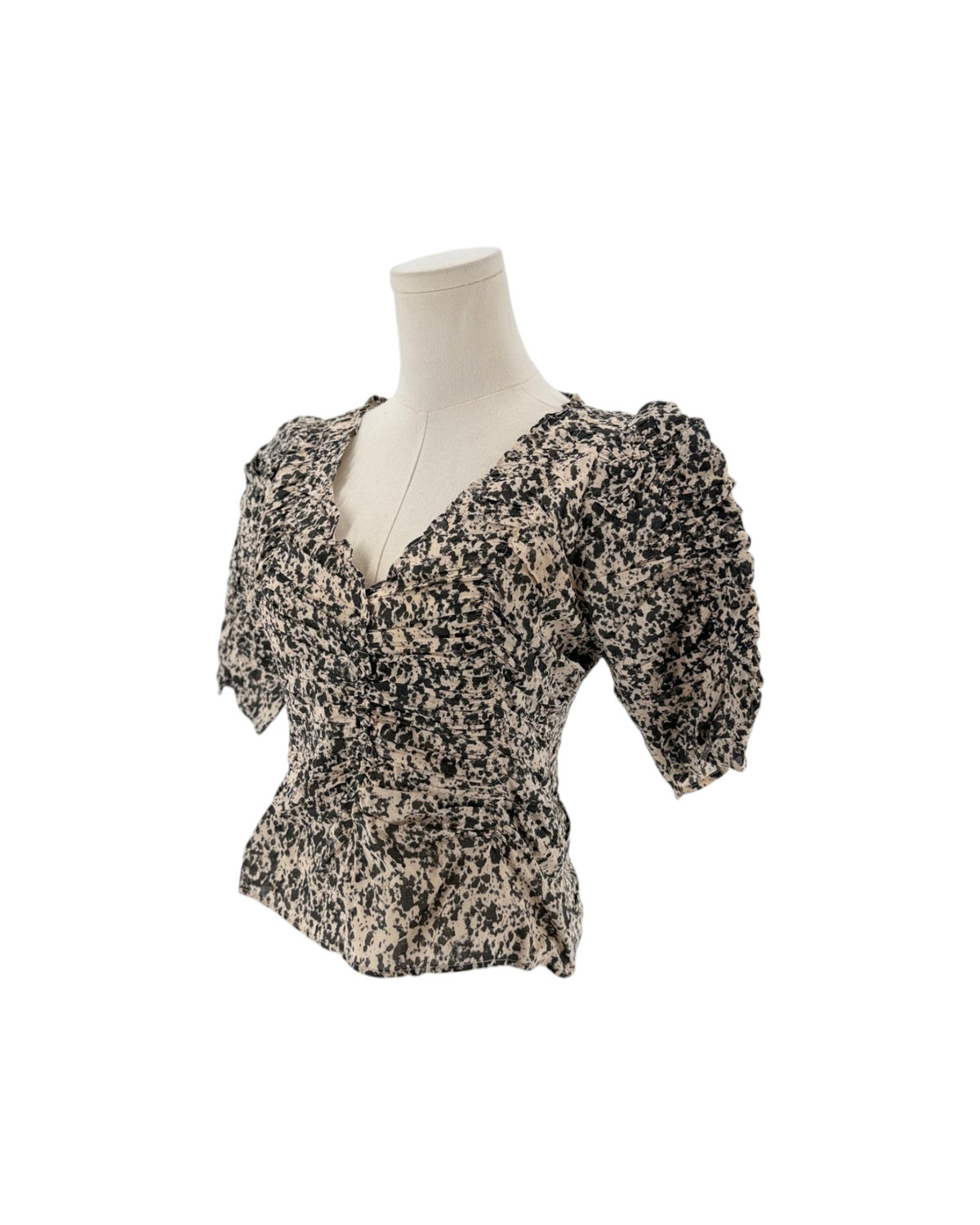 A short-sleeve blouse with puff sleeves and a ruffled peplum hem, featuring a black and beige speckled pattern, displayed on a cream mannequin torso against a white background.