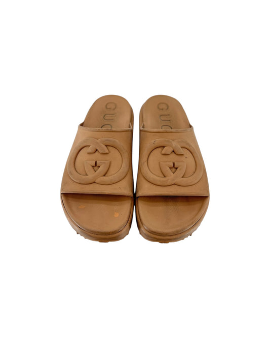 A pair of tan leather slide sandals with the brand name 'GUCCI' embossed on the sole, shown from a top-down view on a white background.

