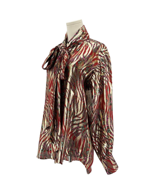 A long-sleeve blouse with an abstract zebra-like pattern in red, brown, black, and beige, featuring a tie-neck detail, displayed on a mannequin torso against a white background.
