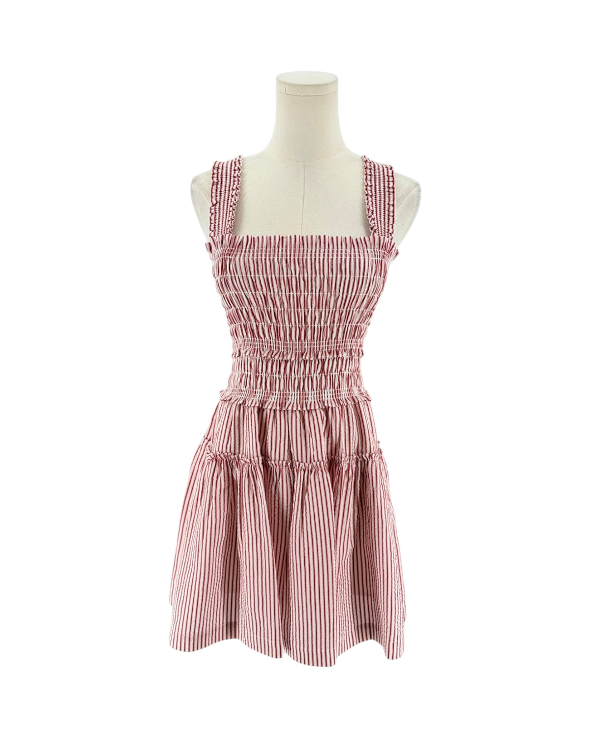 A sleeveless smocked dress with tie shoulder straps, featuring a striped red and white print on a white background, displayed on a mannequin torso against a white background.
