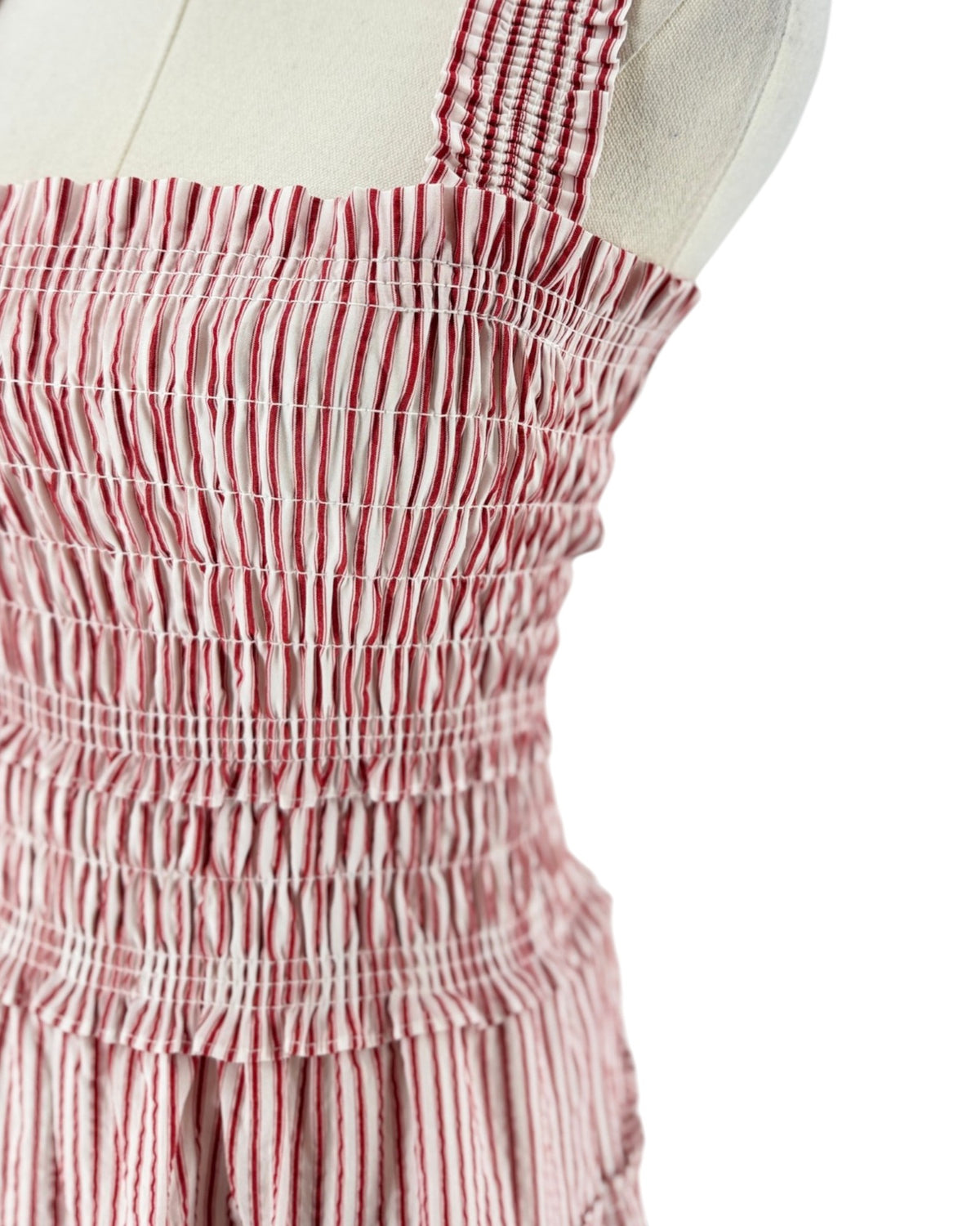 A sleeveless smocked dress with tie shoulder straps, featuring a striped red and white print on a white background, displayed on a mannequin torso against a white background.