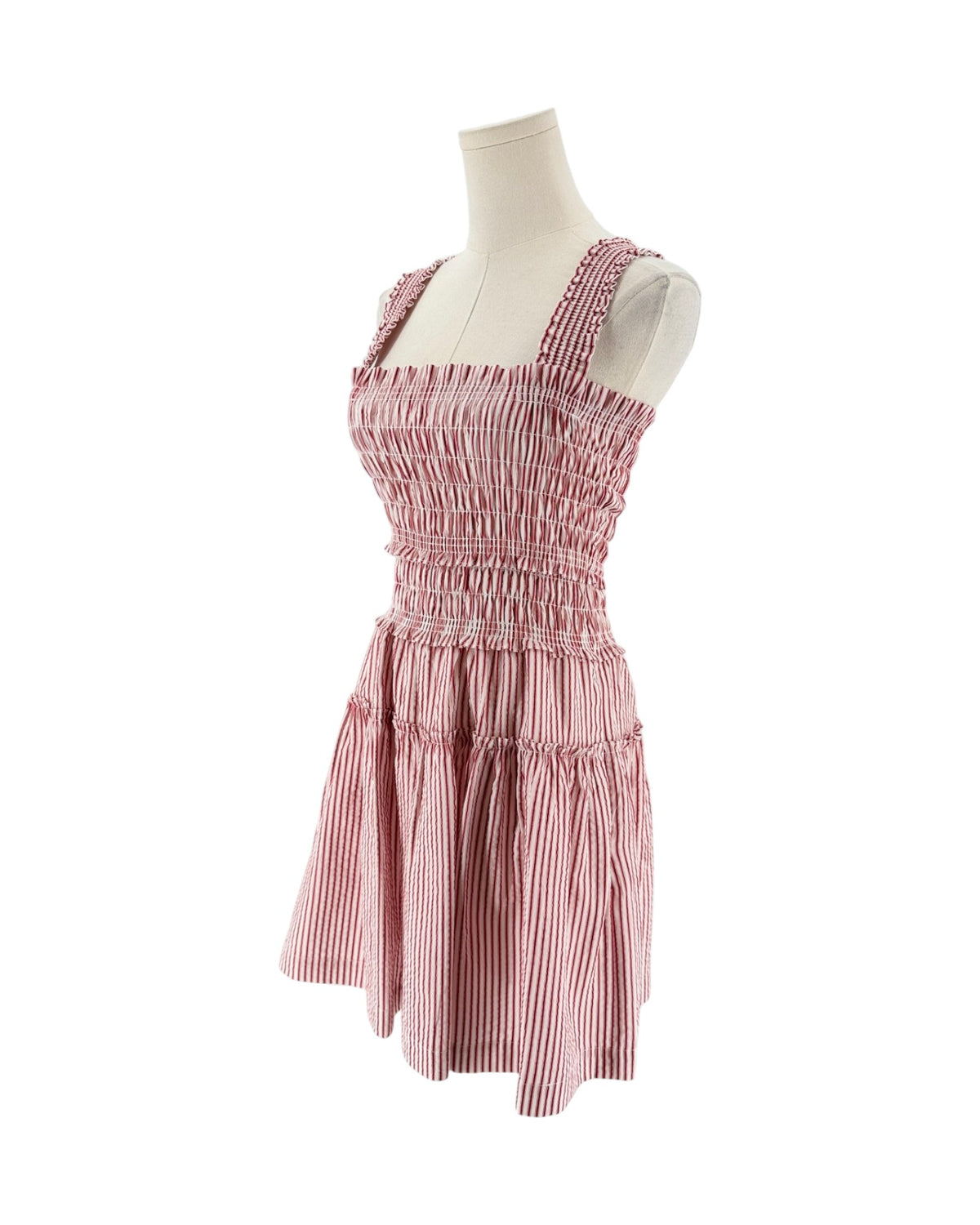 A sleeveless smocked dress with tie shoulder straps, featuring a striped red and white print on a white background, displayed on a mannequin torso against a white background.