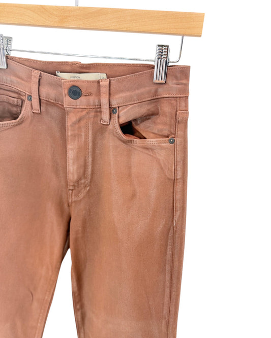 A pair of slim-fit jeans in a washed brown or tan color, hanging from a wooden hanger with metal clips against a plain white background.