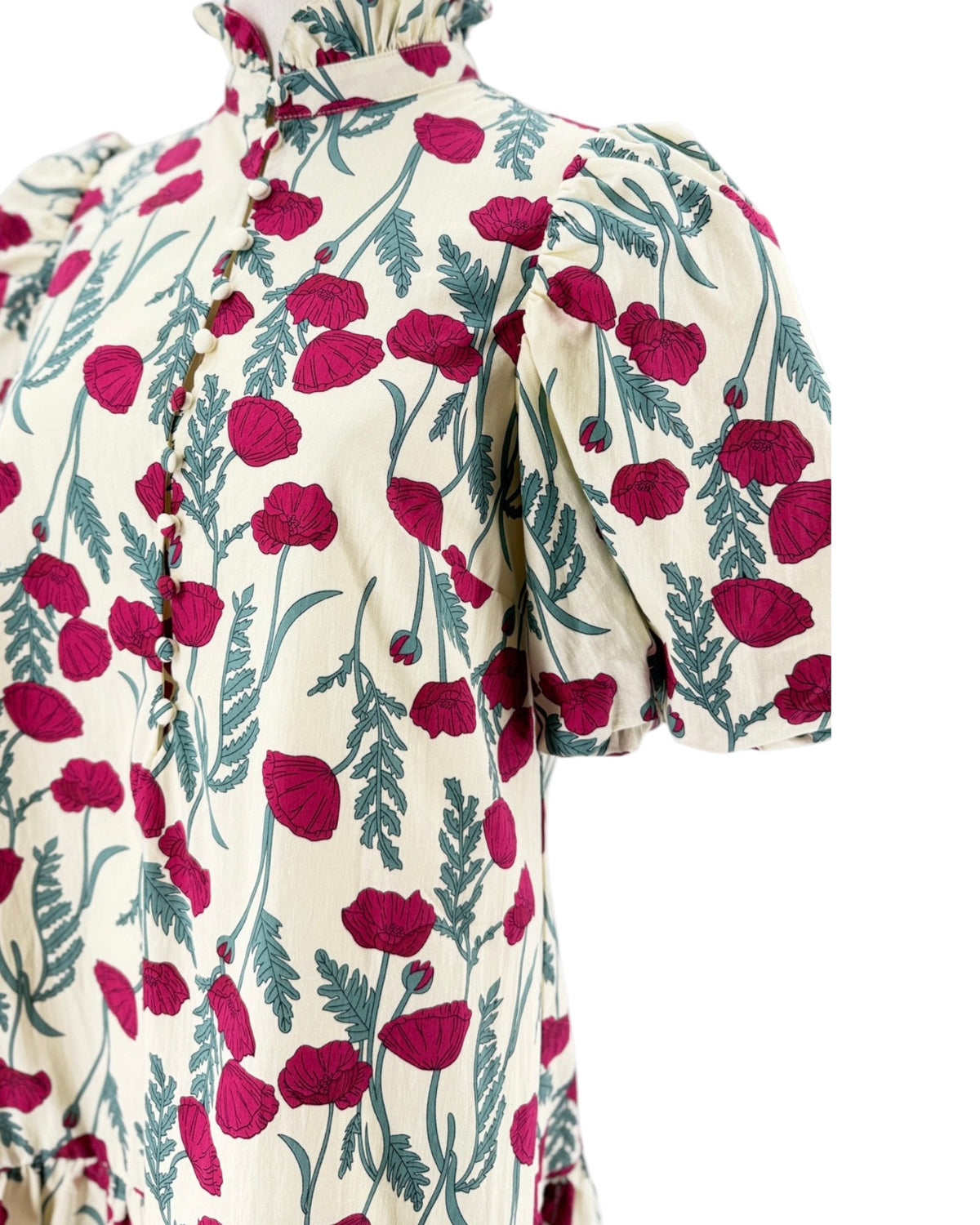 A close-up of a cream-colored dress with a vibrant magenta poppy and green leaf pattern, featuring puff sleeves and a ruffled high neck.