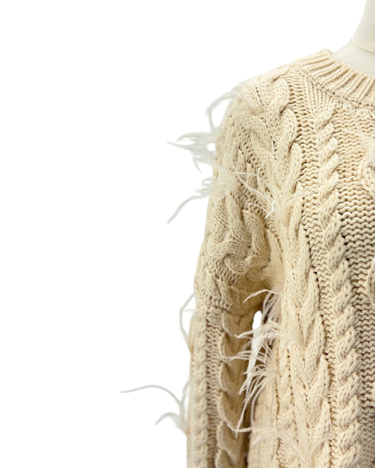 Beige knitted sweater with feather details on a mannequin against a white background