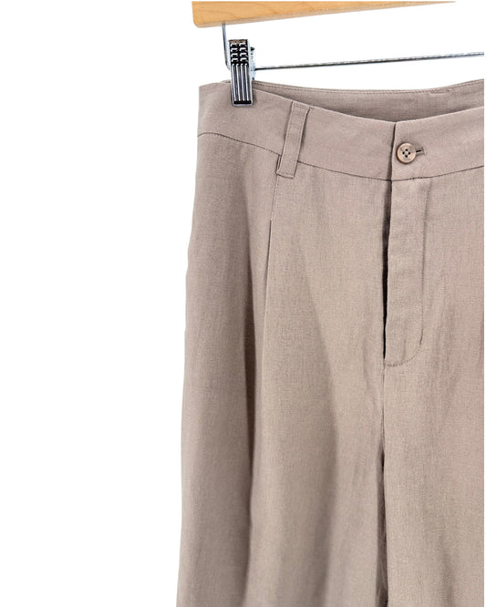Close-up of beige linen shorts hanging from a wooden hanger with a metal clip, showing the waistband, front fly, and side pocket on a white background.