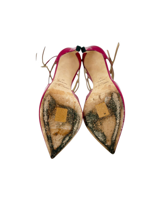 A pair of pointed-toe slingback heels shown from the sole, featuring a bright pink upper and a heavily worn, patched beige and black rubber sole.