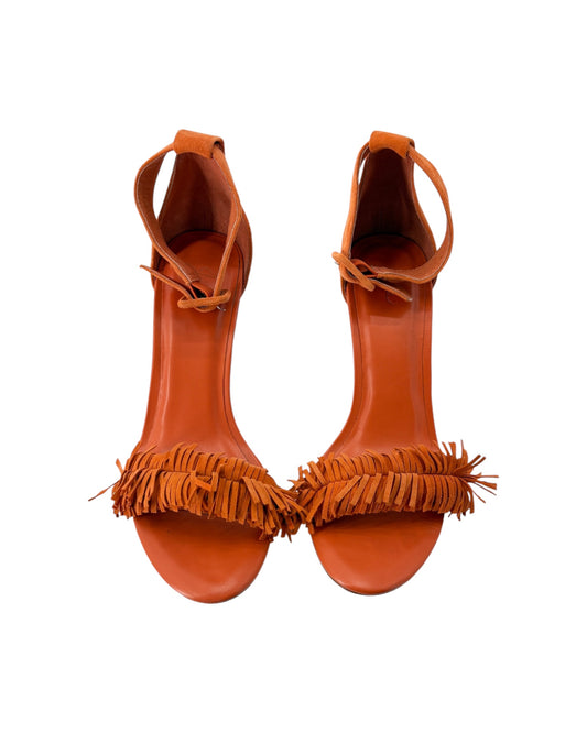 Pair of orange high-heeled sandals with fringe details on a white background