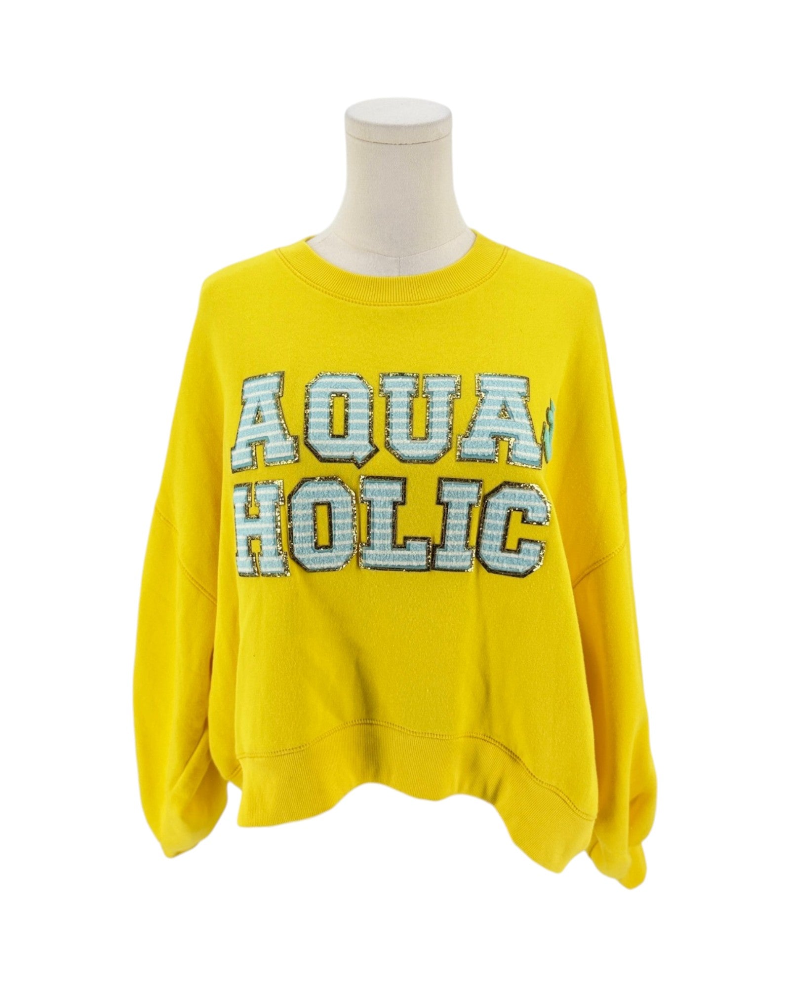 A bright yellow crewneck sweatshirt displayed on a white mannequin torso against a plain white background. The front features the words 'AQUA HOLIC' in large varsity-style block letters with a light blue and white patterned fill and a dark outline.