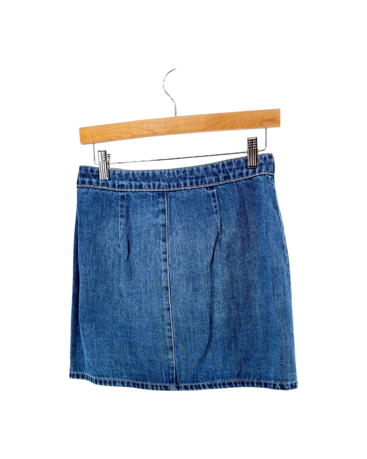 A blue denim mini skirt with a front pleat detail, hanging from a wooden hanger with metal clips against a plain white background.
