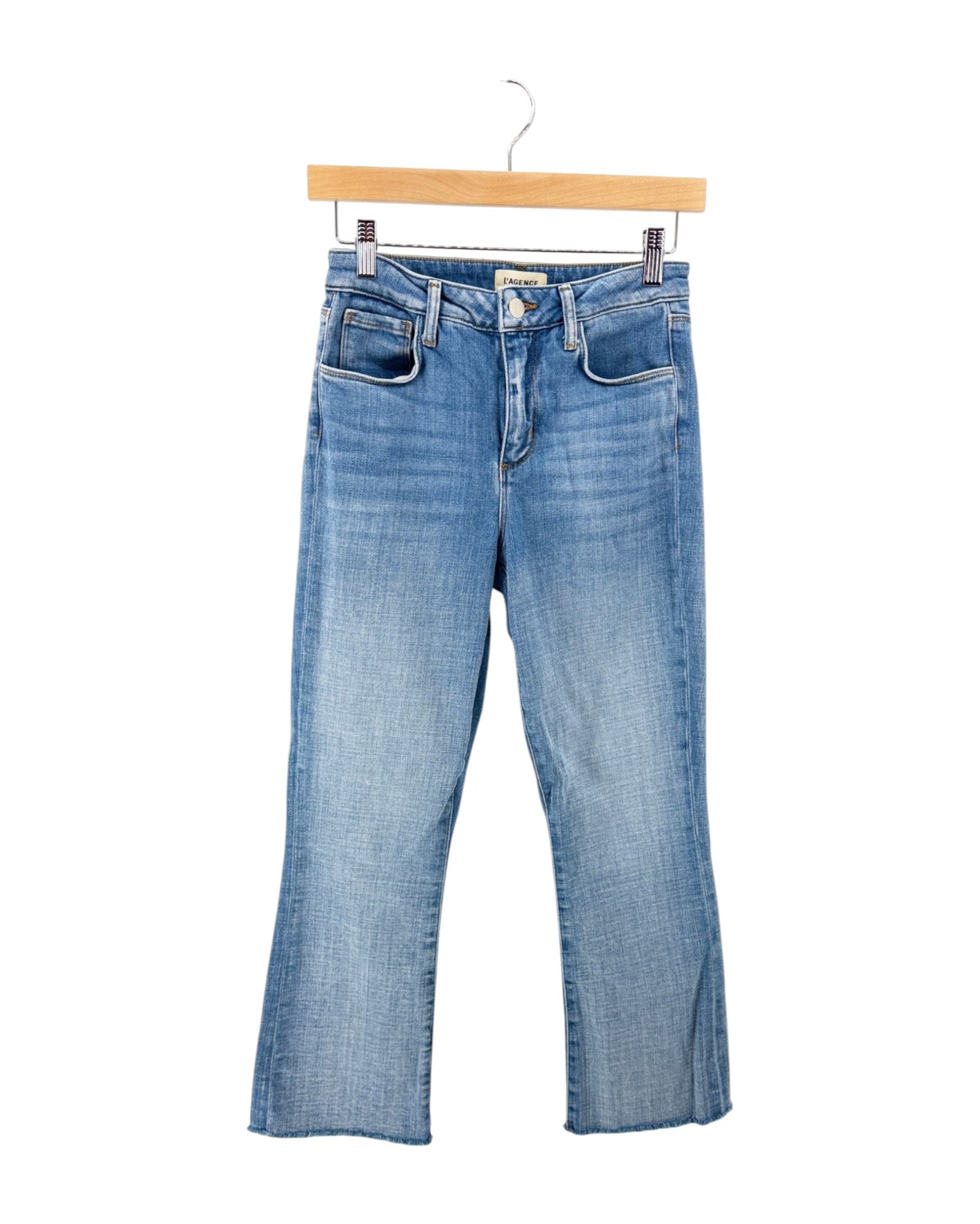 Light blue denim jeans with a subtle wash, featuring a five-pocket design and a straight-to-flared leg, hanging on a wooden hanger against a white background.