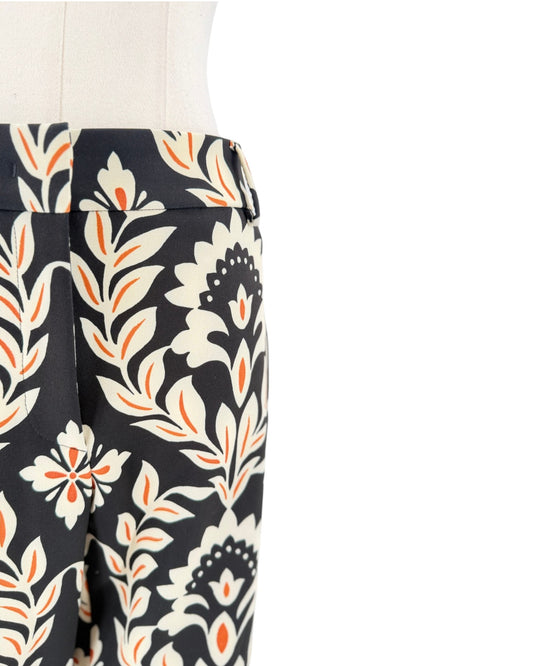Close-up of a pair of trousers on a mannequin, featuring a black base with a cream and orange botanical floral pattern.